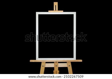 An artistic easel with a picture in white frame isolated on black background. The information frame is mounted on a tripod. Free space for text and image.