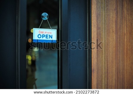 The sign with word “Open” hanging on the glass beside the wooden door in front of the restaurant.
