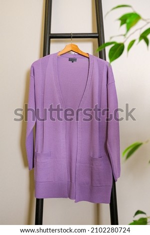 A lilac casual cardigan hanging on black portable stairs leaned on a grey wall Royalty-Free Stock Photo #2102280724