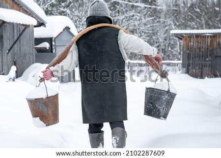 a farmer woman carries a yoke on her shoulders with buckets in which snow lies. technology of water extraction in the winter season. background picture. selective focus.