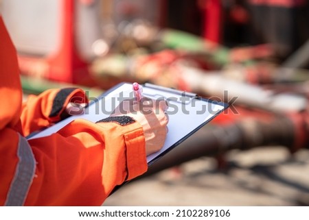 Safety officer or Supervisor is writing note on the checklist paper during perform audit and inspection in oil field operation. Close-up action and selective focus photo.