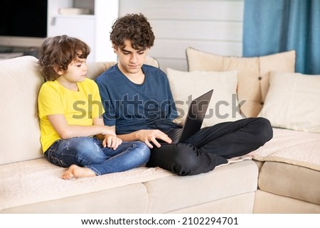 Two brothers sit at home on the couch and look at the laptop. High quality photo