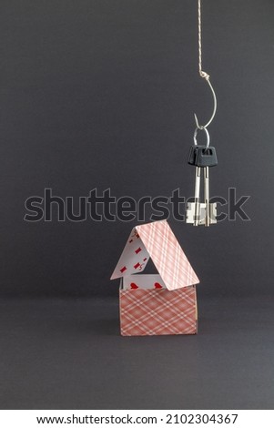 the keys to the house hang like bait on a fishing hook above the house of cards. background picture. space for printing text.