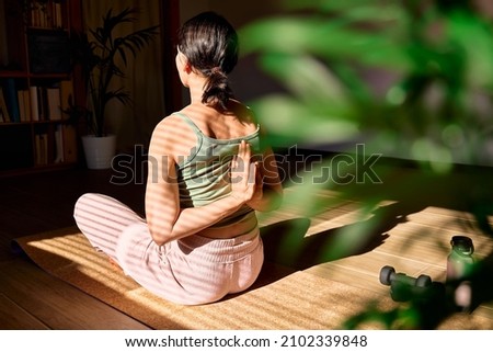 Woman doing Gomukhasana or Cow Face Pose sitting in lotus pose on yoga mat. Wellbeing. Mindful meditation concept. Wellbeing. Practicing yoga at home. Royalty-Free Stock Photo #2102339848