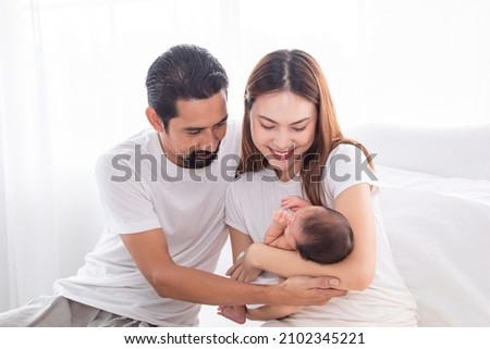 Selective focus of Asian man and woman holding newborn baby in bed at home. Happy family smiling with adorable infant, young parents holding little sweet toddler baby, mom hold toddler with love.
