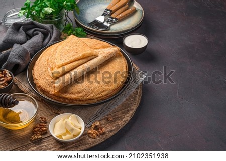 A stack of fried thin pancakes on a dark background. Pancake day. Side view, copy space.