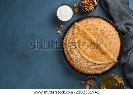 A stack of fried pancakes on a dark background with butter, honey and sour cream. Maslenitsa, Russian blini. Top view.