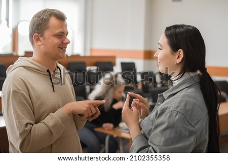The girl and the guy talk in sign language. Two deaf students chatting in a university class.