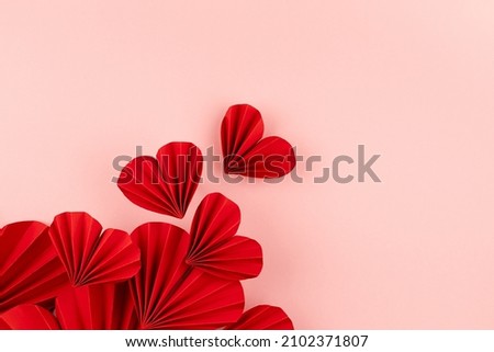 Valentine day background with flow of flying red paper ribbed hearts on soft light pink background as festive backdrop, top view, copy space, border.