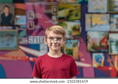 A joyful boy in an art gallery smiles and poses against a background of paintings in the exhibition hall.