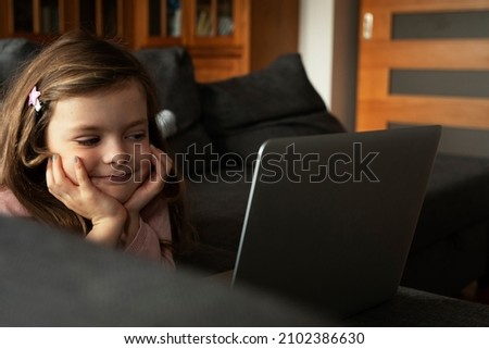 Cheerful little girl using laptop. Beautiful girl watching cartoon on laptop	