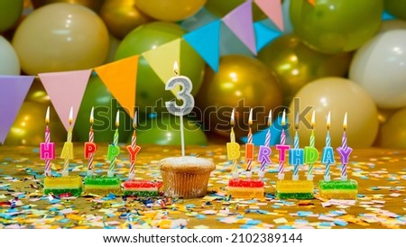 Greeting colorful card happy birthday to the child 3 years old, birthday cupcake with candles and birthday decorations on the background. Copy space