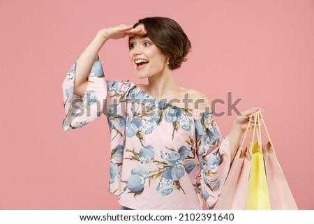 Young woman 20s short hairdo wear trendy stylish blouse holding package bags with purchases after shopping keep hand at forehead look far away distance seek isolated on pastel pink background studio