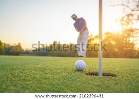 Blurred Golfer putting ball on the green golf, lens flare on sun set evening time. Golfer action to win after long putting golf ball in to the hole.