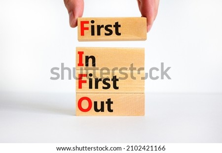 FIFO first in and out symbol. Concept words FIFO first in first out on wooden blocks. Beautiful white table, white background. Businessman hand. Business FIFO first in and out concept. Copy space.