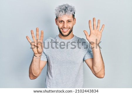 Young hispanic man with modern dyed hair wearing casual grey t shirt showing and pointing up with fingers number nine while smiling confident and happy. 