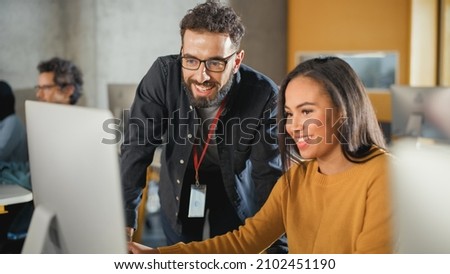 Lecturer Helps Scholar with Project, Advising on Their Work. Teacher Giving Lesson to Diverse Multiethnic Group of Female and Male Students in College Room, Teaching New Academic Skills on a Computer. Royalty-Free Stock Photo #2102451190