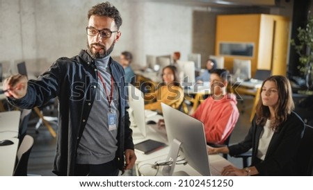 Teacher Giving Lesson to Diverse Multiethnic Group of Female and Male Students in College Room, Learning New Academic Skills on a Computer. Lecturer Shares Knowledge with Smart Young Scholars. Royalty-Free Stock Photo #2102451250