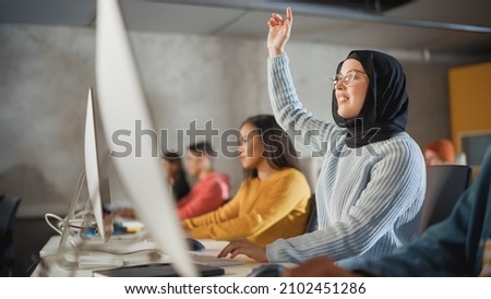 Smart Muslim Female Student in Hijab Studying in University with Diverse Multiethnic Classmates. She Raises Hand and Asks Teacher a Question. Applying Her Knowledge to Acquire Academic Skills in Class