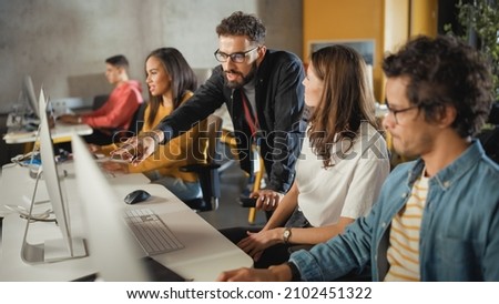 Lecturer Helps Scholar with Project, Advising on Their Work. Teacher Giving Lesson to Diverse Multiethnic Group of Female and Male Students in College Room, Teaching New Academic Skills on a Computer. Royalty-Free Stock Photo #2102451322