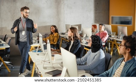 Teacher Giving Lesson to Diverse Multiethnic Group of Female and Male Students in College Room, Learning New Academic Skills on a Computer. Lecturer Shares Knowledge with Smart Young Scholars. Royalty-Free Stock Photo #2102451385