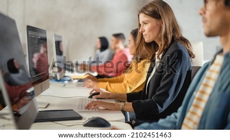 Diverse Multiethnic Group of Female and Male Students Sitting in College Room, Learning Computer Science. Young Scholars Study Information Technology on Computers in University, Writing Code in Class. Royalty-Free Stock Photo #2102451463