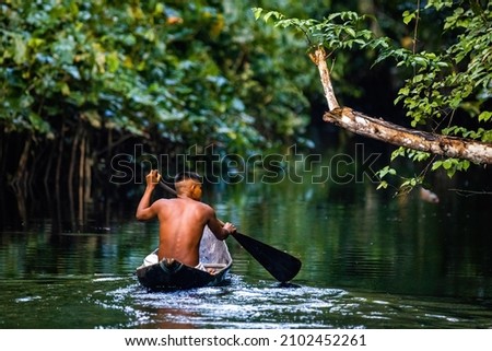 Native tribal man swimming in amazonia rainforest in handmade boat Royalty-Free Stock Photo #2102452261
