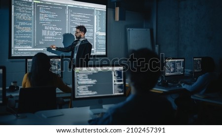Teacher Giving Computer Science Lecture to Diverse Multiethnic Group of Female and Male Students in Dark College Room. Projecting Slideshow with Programming Code. Explaining Information Technology. Royalty-Free Stock Photo #2102457391