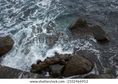 Sea stones top view. Aerial view of the grey seething sea surf. Big foaming waves break on the shore. Neutral natural background for the design. Drone view of the beach huge rocks. Tropical climate