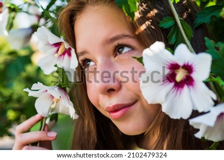 cheerful kid girl among blossoming hibiscuc flower in spring, beauty