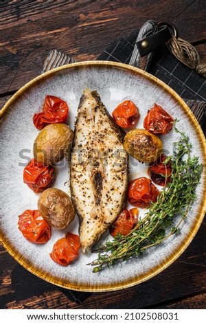 Grilled halibut fish steaks with tomato and potato in plate. Wooden background. Top view