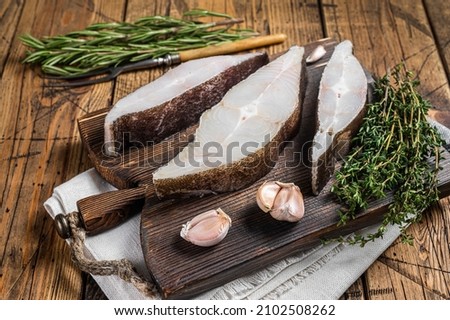 Atlantic halibut fish, raw steaks on wooden board with herbs. Wooden background. Top view
