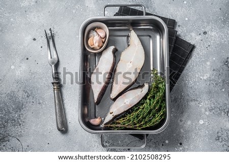 Fresh steak of raw fish halibut in kitchen tray with herbs. Gray background. Top view