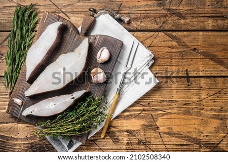 Atlantic halibut fish, raw steaks on wooden board with herbs. Wooden background. Top view. Copy space