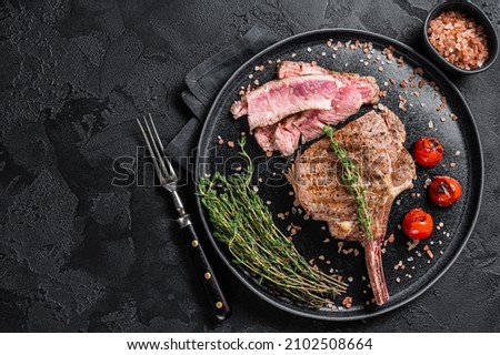 Barbecue sliced rib eye Tomahawk beef veal steak on a plate with pink salt. Black background. Top view. Copy space Royalty-Free Stock Photo #2102508664