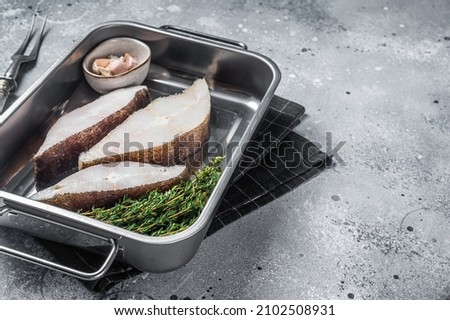 Fresh steak of raw fish halibut in kitchen tray with herbs. Gray background. Top view. Copy space