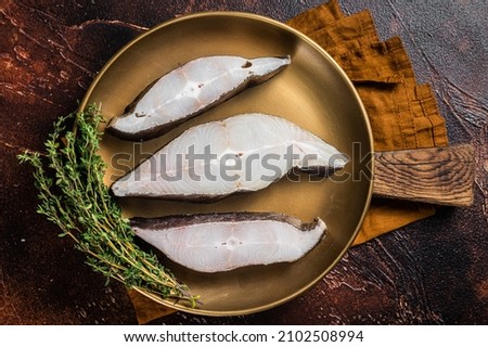 Sliced halibut fish, raw steaks on plate with thyme. Dark background. Top view