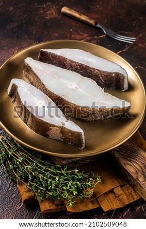 Sliced halibut fish, raw steaks on plate with thyme. Dark background. Top view
