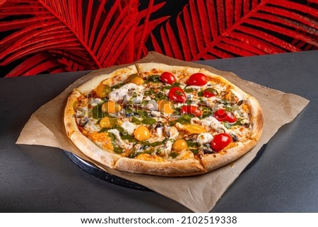 pizza with cheese, mushrooms, red and yellow tomatoes, chicken on a wooden board on a dark stone background