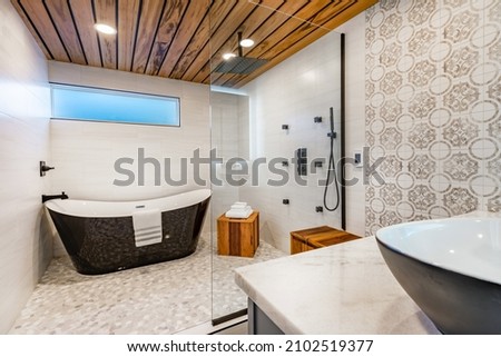 Spacious bathroom with tub and shower in enclosure glass walls black bathtub tiger wood accents decorative tile and mosaic floor tile Royalty-Free Stock Photo #2102519377