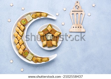 Traditional middle eastern dessert baklava in shape of moon and star . Ramadan background with sweets and lantern   , Top view, flat lay , copy space                          Royalty-Free Stock Photo #2102558437