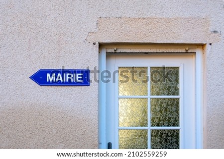 Blue directions sign with the word "town hall" written on it in French language, and attached to a wall next to an entrance door