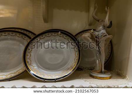 Old white decorative plates standing on shelf and statue of dancing woman