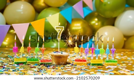 Happy birthday greeting card to a 7 year old child, birthday cupcake with candles and birthday decorations on the background. Copy space