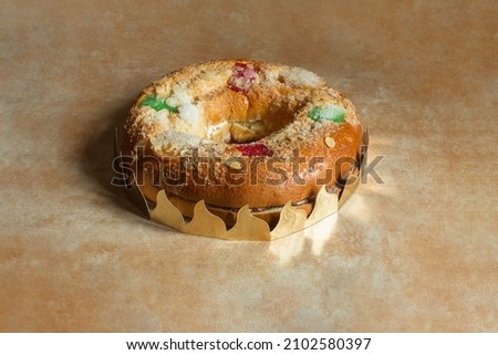 Large donut cake filled with sweet whipped cream and meringue with candied fruit, almonds, sugar, surrounded by a wreath on a textured abstract design table. Traditional sweets dessert on holidays.