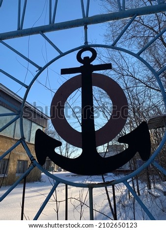 relief of the anchor on a gray background visible through the fence in the winter through snow with a dry autumn leaf