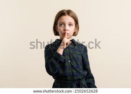 Strabismus Kid Little Girl 9s Wearing Plaid Shirt Dress making silence gesture with finger on his lips. Child have a crossed eye. Health problem. Healthcare And Medicine Concept Royalty-Free Stock Photo #2102652628