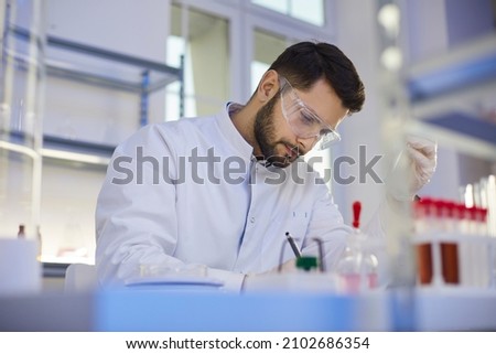 Young professional man lab assistant in medical uniform glasses work with test glass tubes do research in laboratory. Male scientist make chemistry experiments. Science, biotechnology concept. Royalty-Free Stock Photo #2102686354