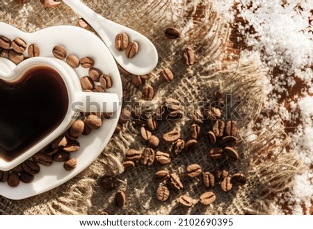 Cup of coffee in the shape of a heart on a snowy wooden table. Coffee beans. Winter morning coffee