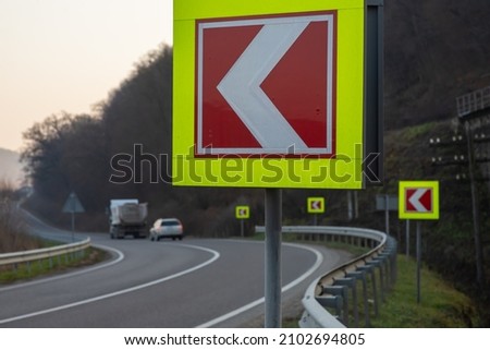 Asphalt road with bright traffic signs in situ of the sharp left turn.